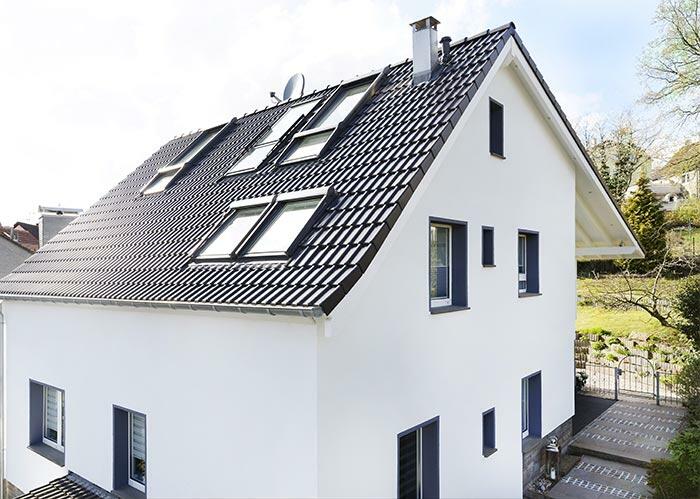 Nowoczesny, biały dom jednorodzinny z czarnym, spadzistym dachem, na którym zamontowano kilka okien dachowych VELUX;